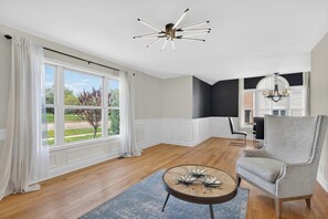 Ein großzügiges Wohnzimmer mit einem großen Fenster, einer modernen Kronleuchter und einem grauen Sessel.