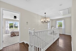 A spacious room with a wooden floor, a white railing, and a chandelier. - Huge 4BR Game Retreat · Sleeps 8 · Chicago (Glendale Heights)