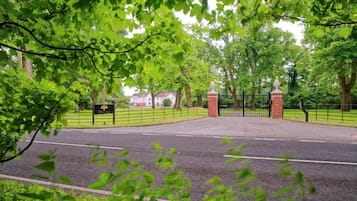 A gated entrance with a brick wall and metal gate, surrounded by lush green trees.