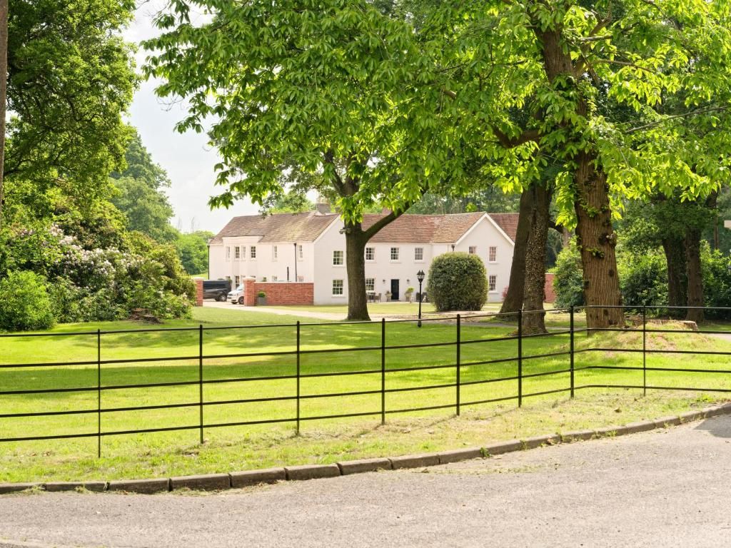 A white building with a brick foundation, surrounded by a well-maintained lawn and a metal fence.