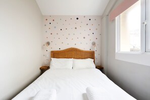 A neatly made bed with white linens, a wicker headboard, and a wall with colorful polka dots. - Bright 1BR Flat near station/easy access to centre (Brighton and Hove)