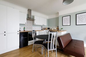 Eine moderne Küche mit weißen Schränken, einem schwarzen Kühlschrank, einem Herd und einer Essecke mit Tisch und Stühlen.