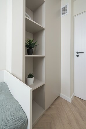 Quarto minimalista com porta branca, estante embutida e um vaso de planta.