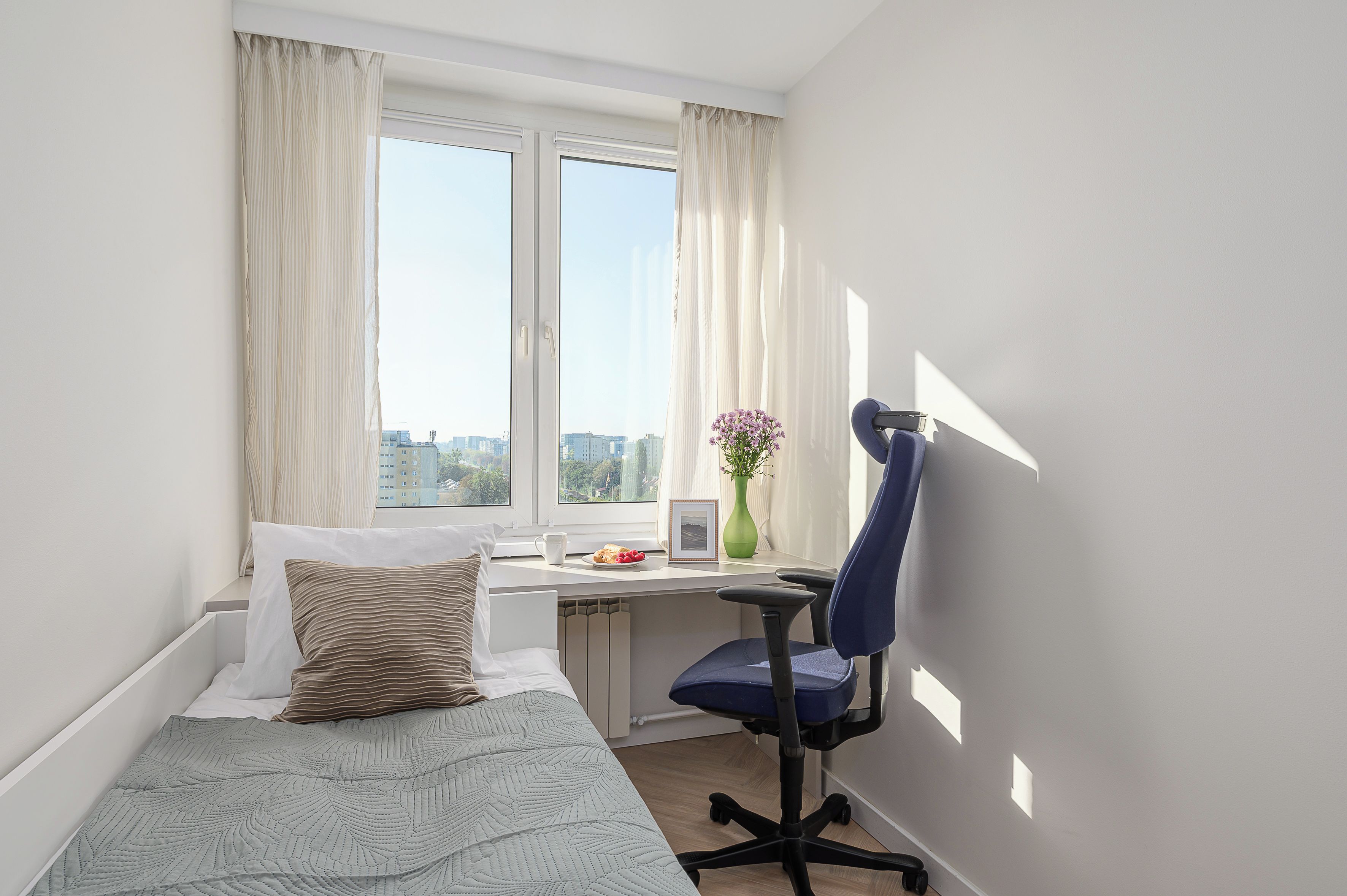 Quarto com cama, escrivaninha, cadeira e janela com cortinas.