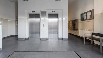 Un'area ascensori moderna con due cabine, una panca e una bacheca informativa a parete.