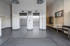 Een modern liftgedeelte met twee liften, een bankje en een informatiebord aan de muur.