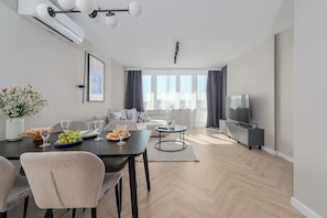 Een moderne woonkamer met een eethoek, een flatscreen televisie en een groot raam met gordijnen.