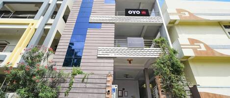 A modern hotel building with a prominent blue stripe, a balcony, and a sign for De Alphabet Luxury Hotels.