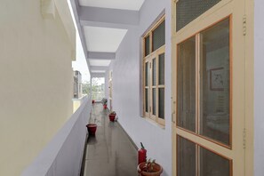 A corridor with potted plants, a fire extinguisher, and a window with a mesh screen.