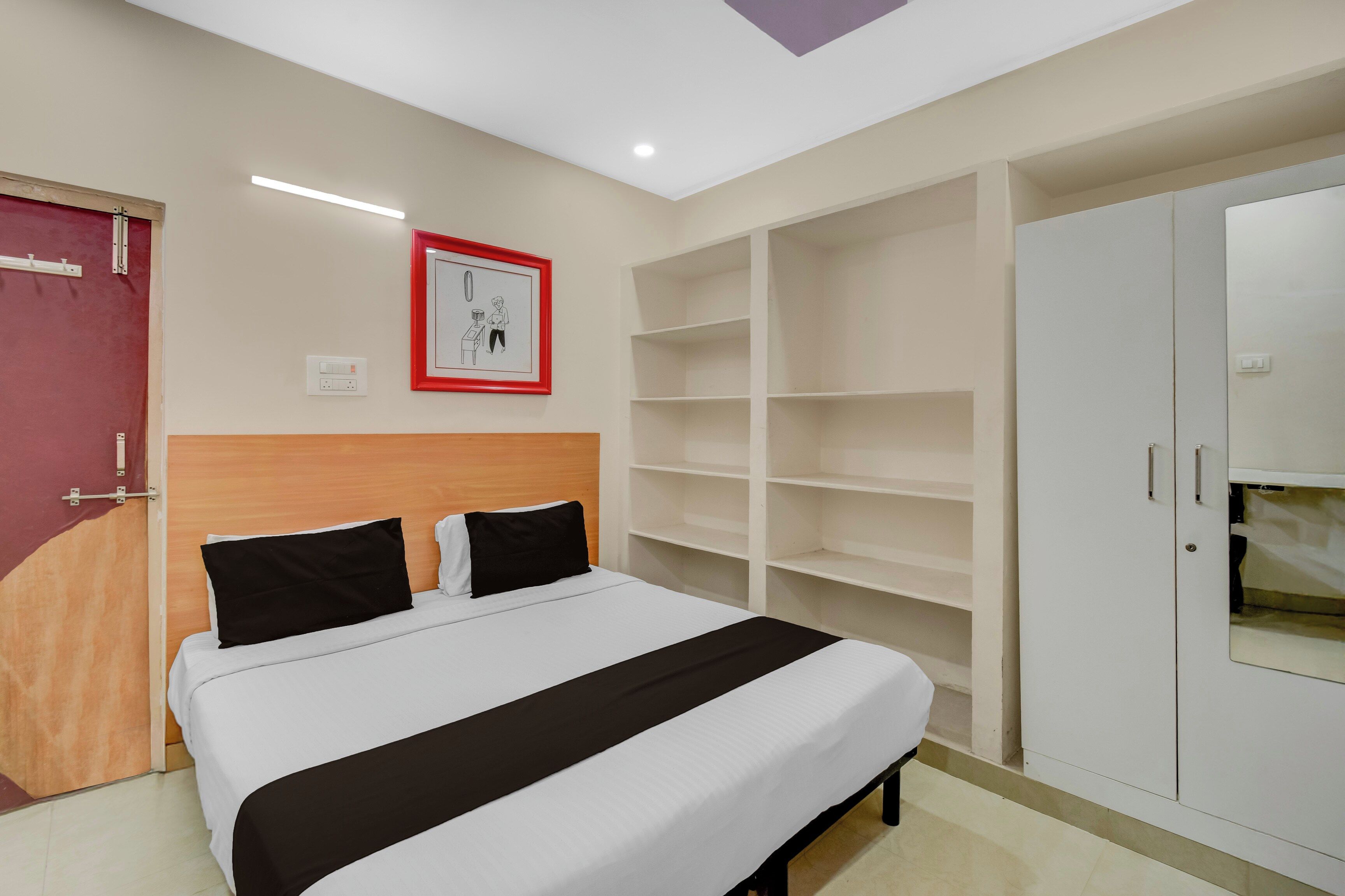 A bedroom with a bed, a wardrobe, a shelf unit, and a wall-mounted light fixture.