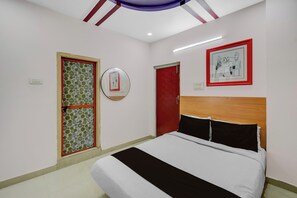 A bedroom with a bed, a door, a mirror, and a framed picture on the wall.
