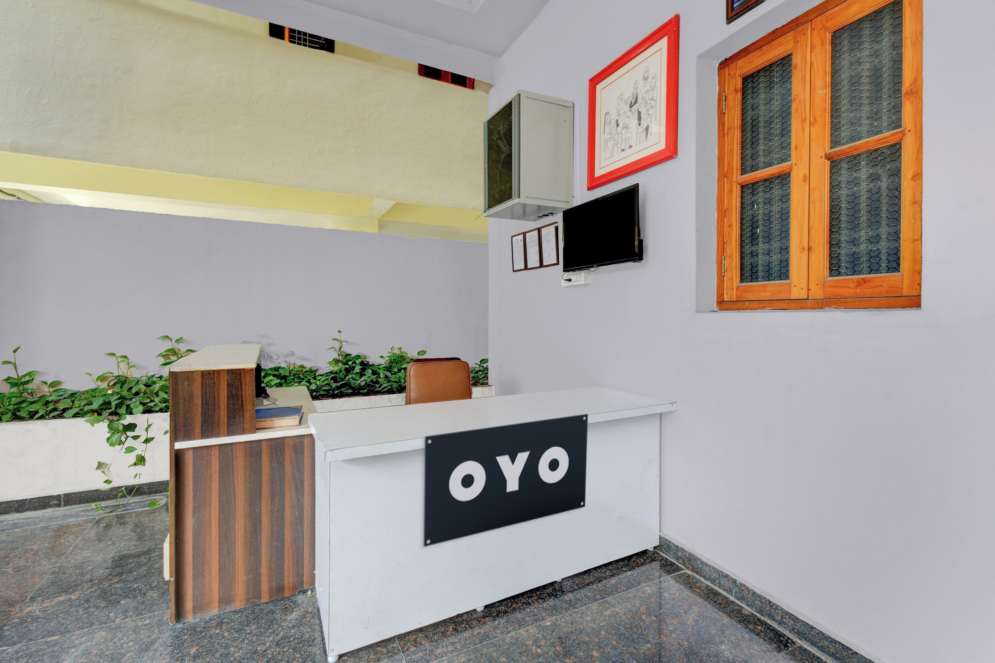 A reception desk with a sign that reads 'OYO,' a mounted television, and a window with a wooden frame.