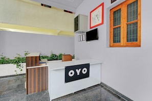 A reception desk with a sign that reads 'OYO,' a mounted television, and a window with a wooden frame. - Hotel O De Alphabet Home Stays NTPC  (Ramagundam)