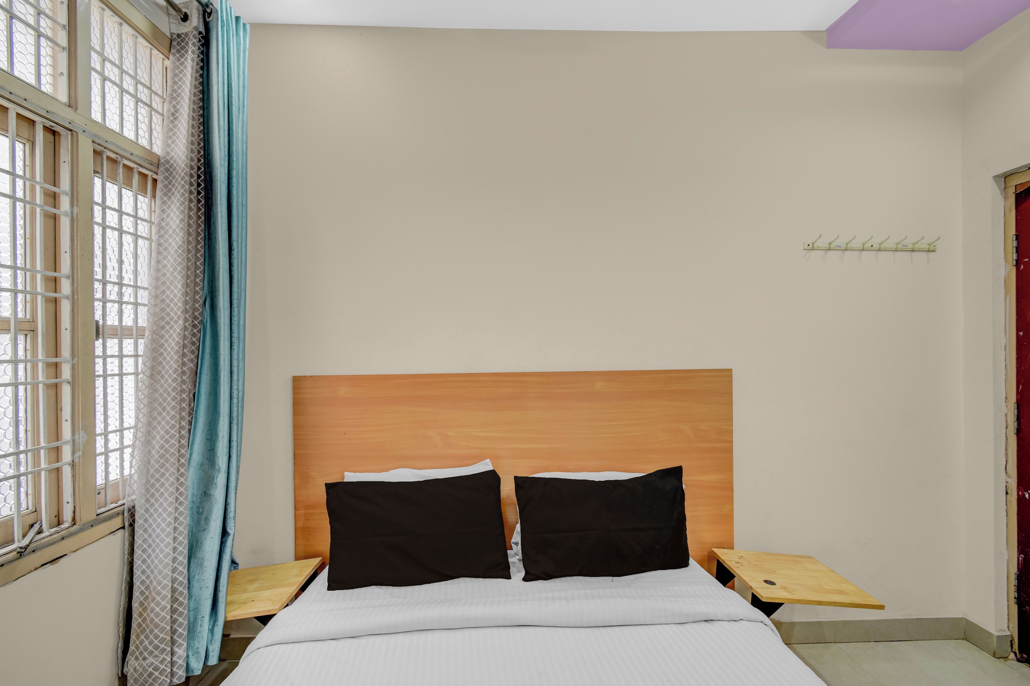 A bedroom with a wooden headboard, two black pillows, a white bedspread, and a wooden nightstand with a hook.