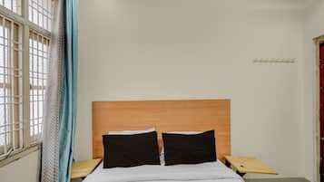 Un dormitorio con cabecera de madera, dos almohadas negras, una colcha blanca y una mesita de noche con un gancho.