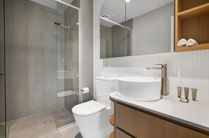 A modern bathroom with a glass shower enclosure, a white toilet, a round sink, and a wooden vanity. - Panoramic 2-bed Apartment Near South Melbourne (Melbourne)