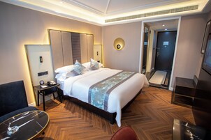 A hotel room with a large bed, a desk with a chair, a bedside table, and a door leading to a bathroom.