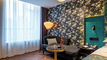 Habitación de hotel con sofá, una mesita redonda, una lámpara decorativa y una cama con colcha estampada.
