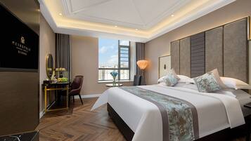 A hotel room with a large bed, a desk with a lamp, a chair, and a view of the city through a window.