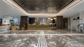 A hotel lobby with a reception desk, a marble floor, and a geometric ceiling design.