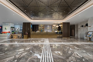 A hotel lobby with a reception desk, a marble floor, and a geometric ceiling design.