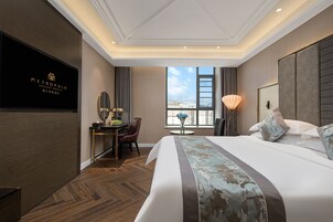 A hotel room with a bed, a desk with a chair, a lamp, and a view of the city.