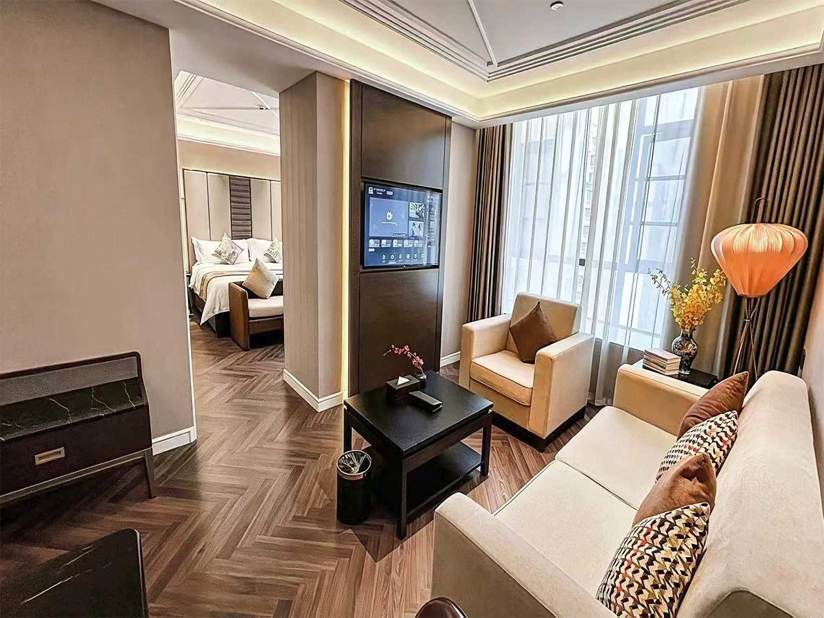 Una habitación de hotel con cama, zona de estar con sofá y sillones, televisión y un ventanal amplio.