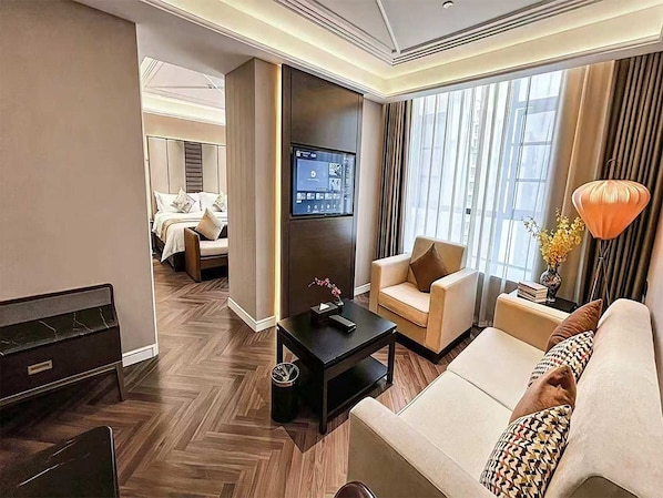 A hotel room with a bed, a seating area with a sofa and armchairs, a television, and a large window.