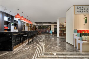 A hotel lobby with a marble floor, a reception desk, and a seating area with chairs.