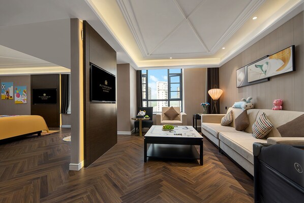 A modern hotel room with a sofa, a coffee table, a TV, and a large window offering a city view.