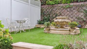 A garden with a fountain, white outdoor furniture, and a brick wall with climbing plants.