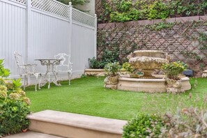 A garden with a fountain, white outdoor furniture, and a brick wall with climbing plants. - Distinguised 4-bedroom townhouse (South Kensington)