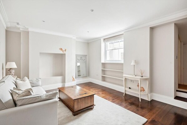 A spacious living room with a wooden coffee table, a sofa, and a white console table. - Distinguised 4-bedroom townhouse (South Kensington)