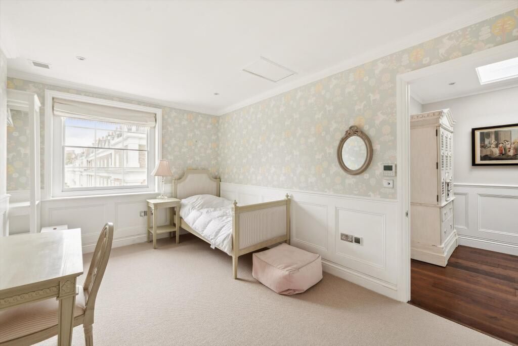 A bedroom with a single bed, a bedside table, a chair, a window, and a door leading to another room.
