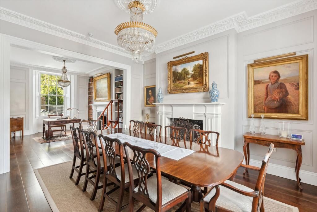 A formal dining room with a large wooden table, ornate chairs, a chandelier, and classical paintings.
