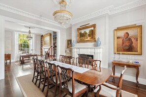 A formal dining room with a large wooden table, ornate chairs, a chandelier, and classical paintings. - Distinguised 4-bedroom townhouse (South Kensington)