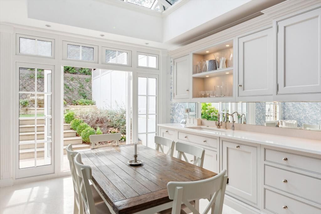 Una cucina luminosa con mobili bianchi, un tavolo da pranzo in legno e vista su un giardino tramite ampie finestre.