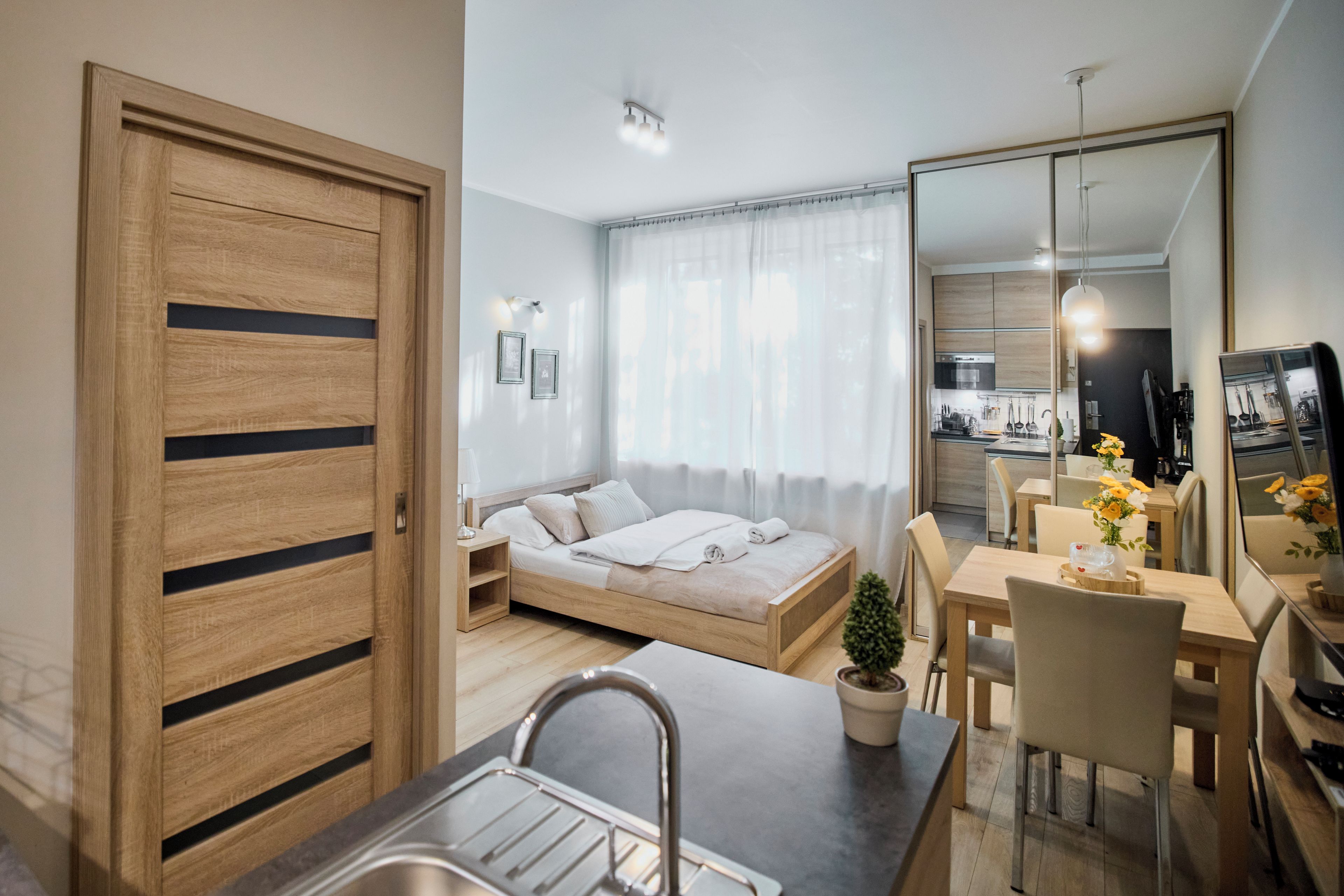 Un espacio habitable moderno y funcional con kitchenette, cama, comedor y un espejo grande.