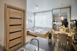 A modern, compact living space with a kitchenette, a bed, a dining area, and a large mirror. - RentPlanet - Apartamenty Piłsudskiego 41 (Wrocław)
