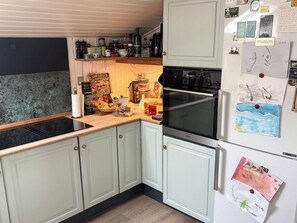 A kitchen with light-colored cabinets, a black stove, and a refrigerator with children's drawings. - 5 Person Holiday Home in Havndal (Havndal)