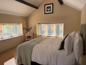 Ein Schlafzimmer mit einem Bett, zwei Fenstern, einem Nachttisch mit Pflanze und einem Bild an der Wand.