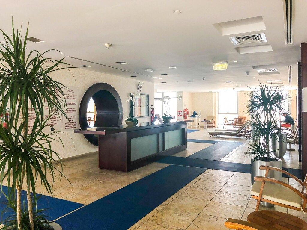 A hotel lobby with a reception desk, seating area, and potted plants.