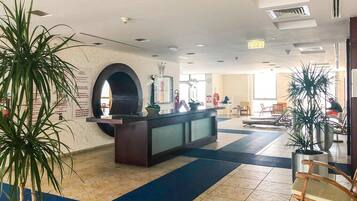 A hotel lobby with a reception desk, seating area, and potted plants.
