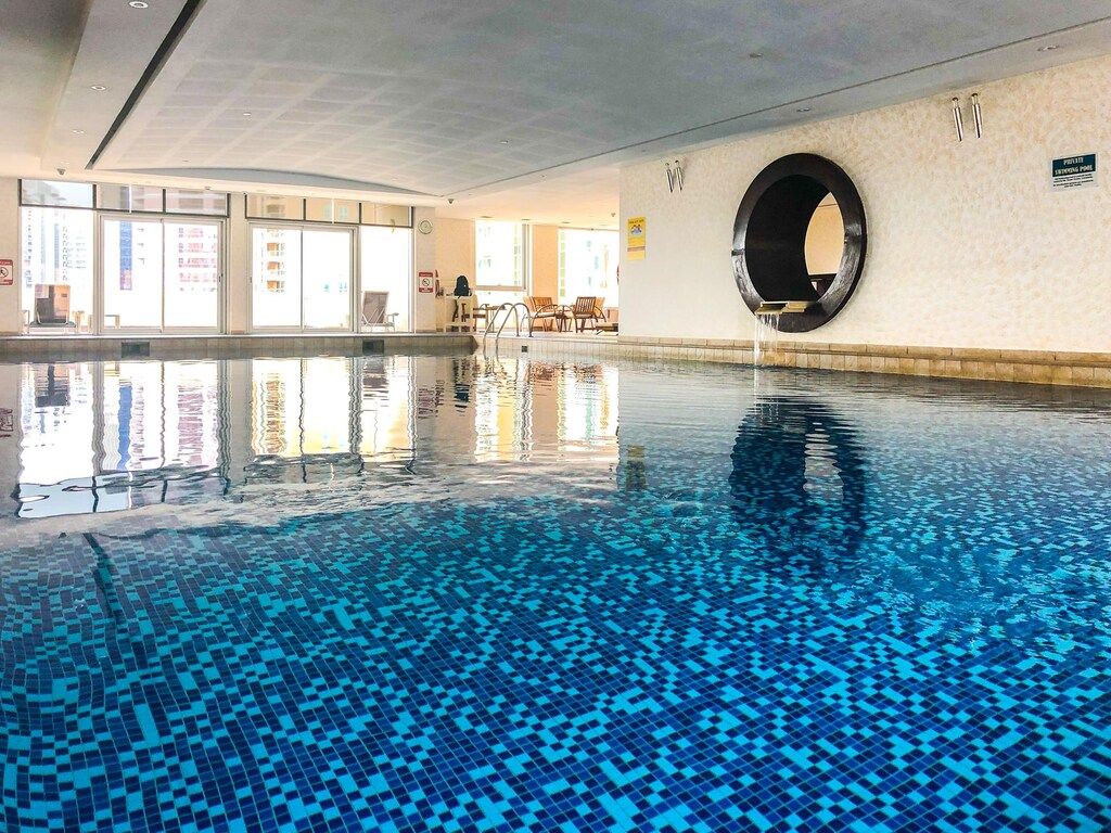 Une piscine intérieure à l’eau claire, une fenêtre circulaire dans le mur et une vue sur l’extérieur grâce à de grandes baies vitrées.