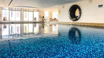 Une piscine intérieure à l’eau claire, une fenêtre circulaire dans le mur et une vue sur l’extérieur grâce à de grandes baies vitrées.