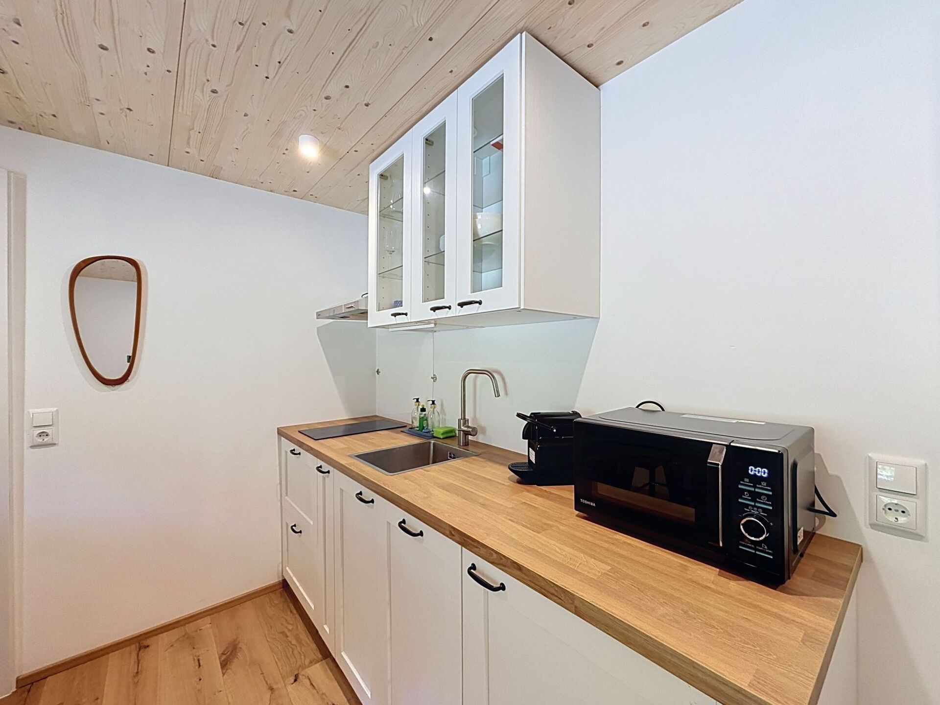 Una cocina compacta con armarios blancos, encimera de madera, microondas negro y un lavamanos.