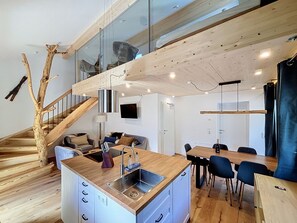 Eine moderne Küche mit einer zentralen Kochinsel, einem Essbereich mit Stühlen und einer Holztreppe.