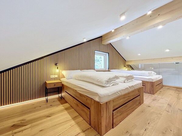 Un dormitorio con techo inclinado, paneles de madera, una cama, una mesita de noche y una ventana.