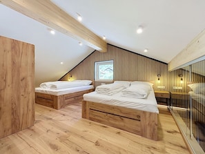 Un dormitorio moderno con dos camas de madera, techo inclinado y un ventanal grande.