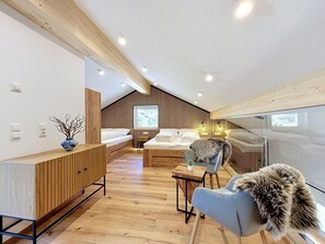 Ein modernes Schlafzimmer mit schrägen Wänden, Holzboden, einem Bett mit weißen Leinen, einer Sitzecke mit Sessel und Tisch sowie einem großen Fenster, das natürliches Licht hereinlässt.